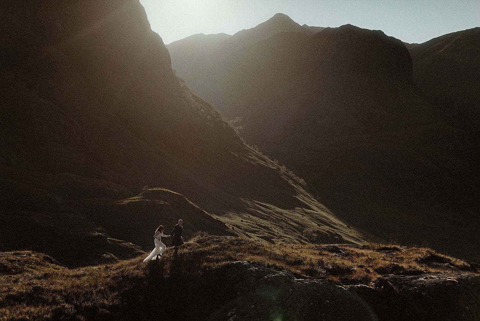 A couple walking in the sunlight between the mountains of Glencoe after their elopement in Scotland