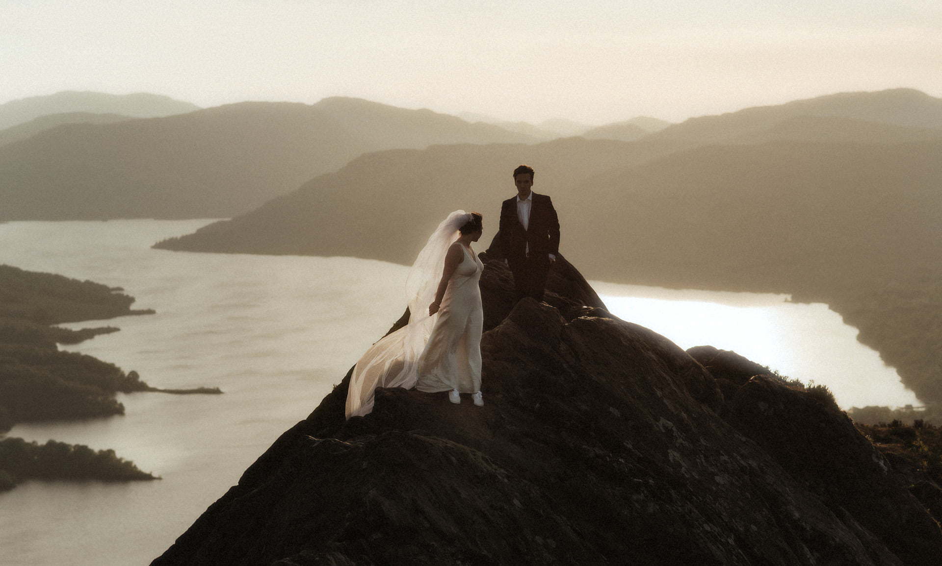 eloping in Scotland Guide with a couple walking in the sun set on top of a mountain