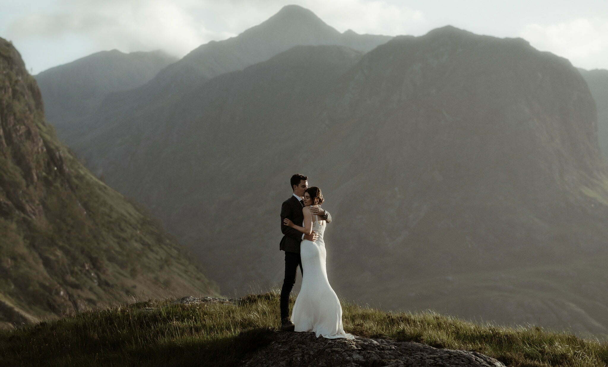 elope in scotland couple standing in the sunshine between the mountains of Glencoe