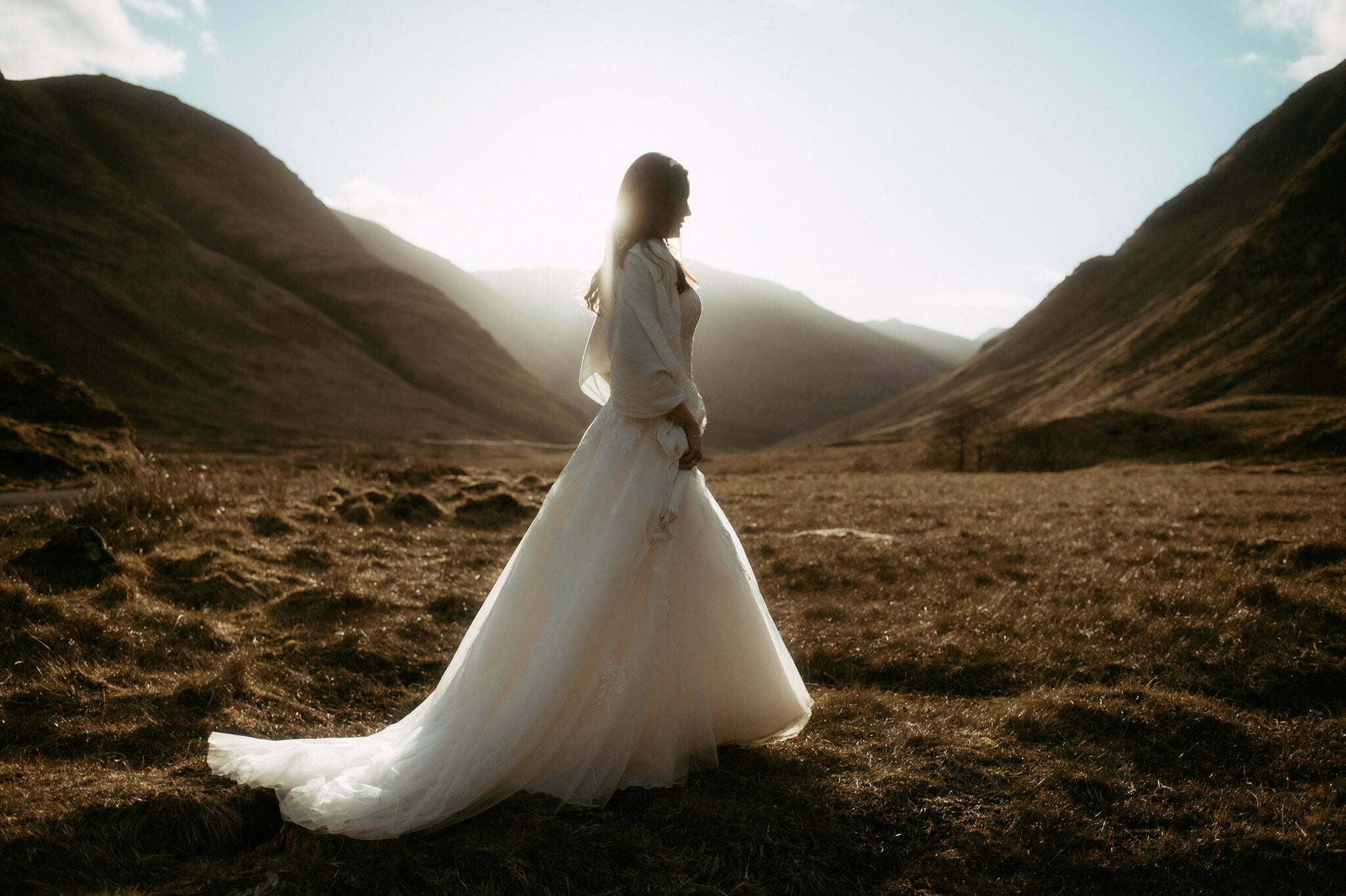 bride walking in the mountains of glencoe with sun behind her