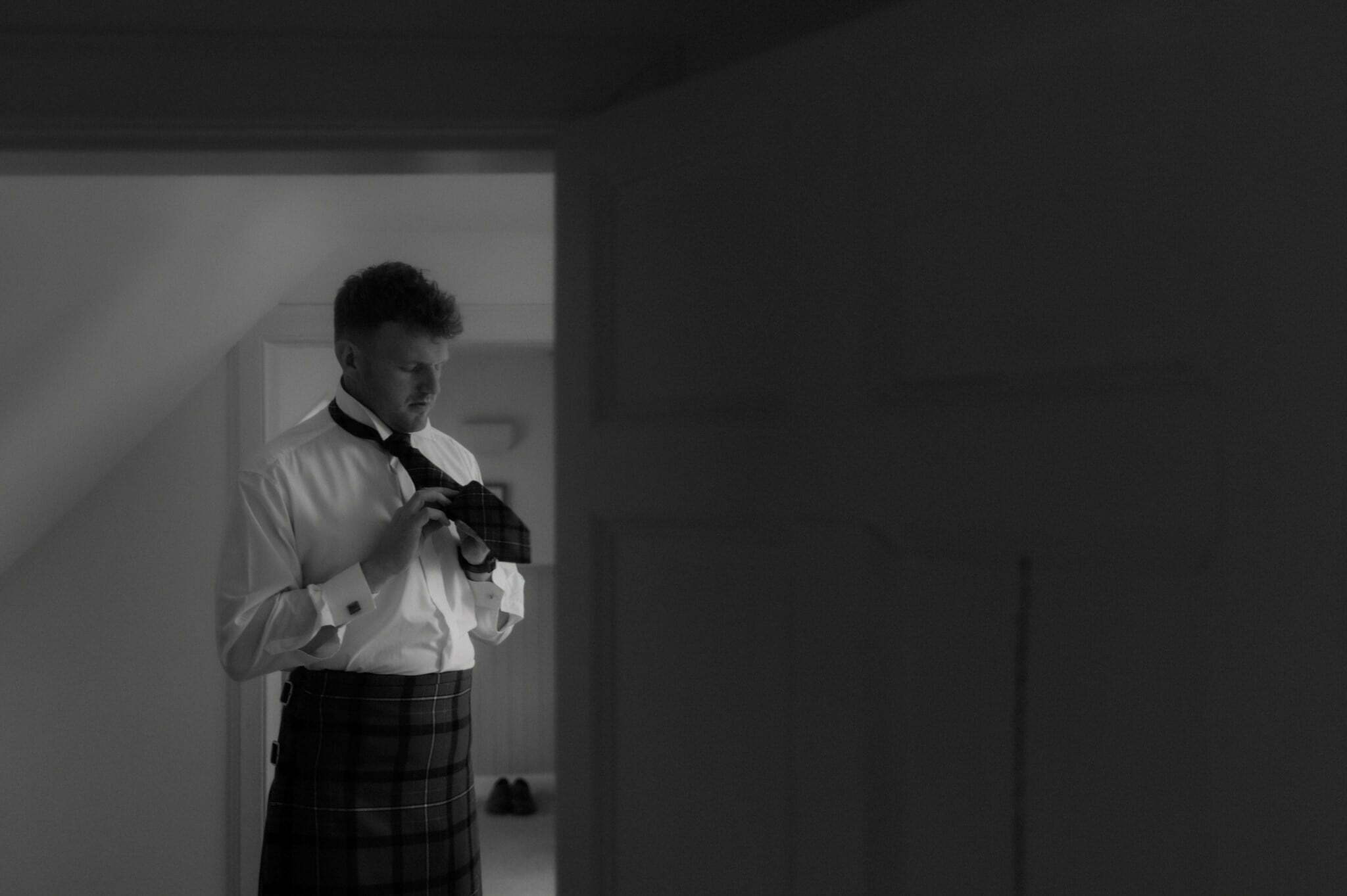groom during his scotland elopement getting ready with kilt and tie