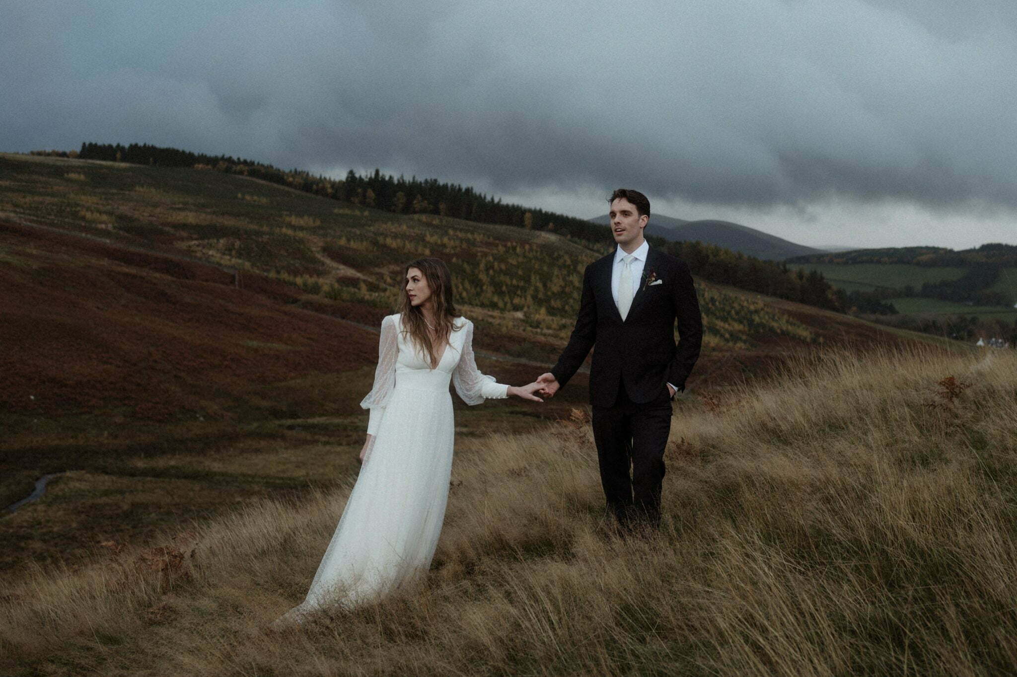 scotland elopement in the scottish borders couple standing in the hills with trees and mountains behind