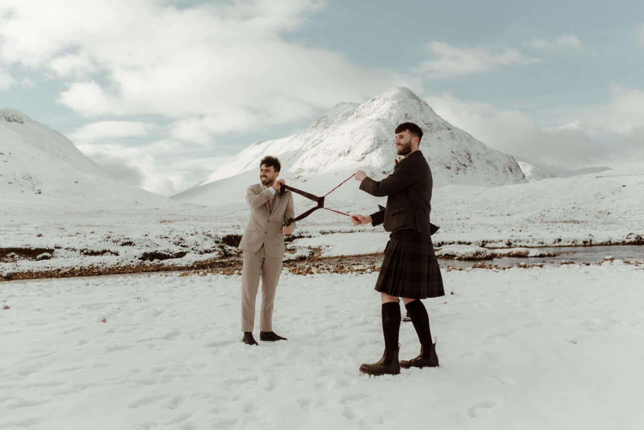gay elopement couple in glencoe after their winter ceremony at the wee white cottage with snow capped mountain