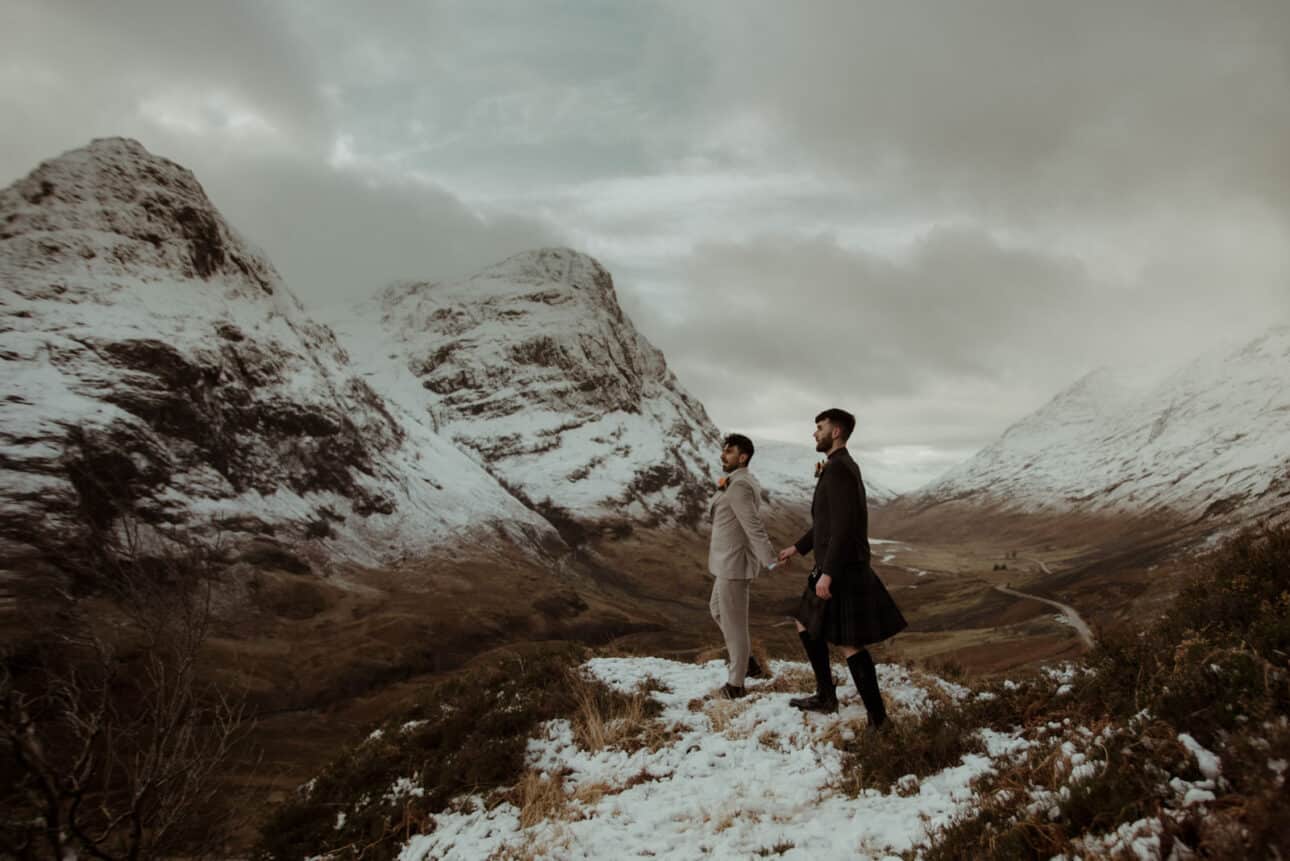 gay elopement couple in glencoe after their winter ceremony at the wee white cottage with snow capped mountain