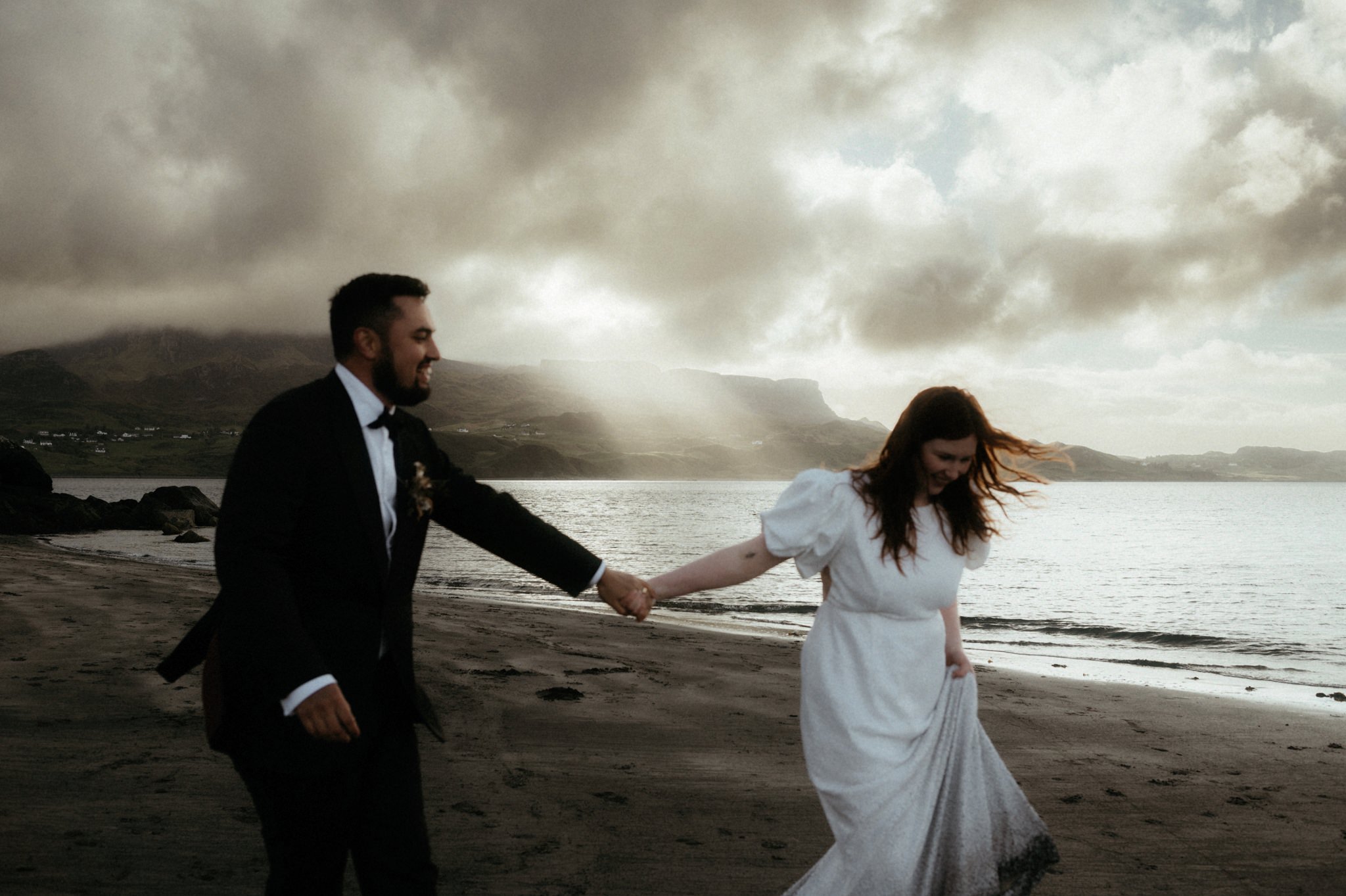 Scotland elopement photographer Sean Bell's image of Bride and Groom walking on Staffin beach with a sunset behind