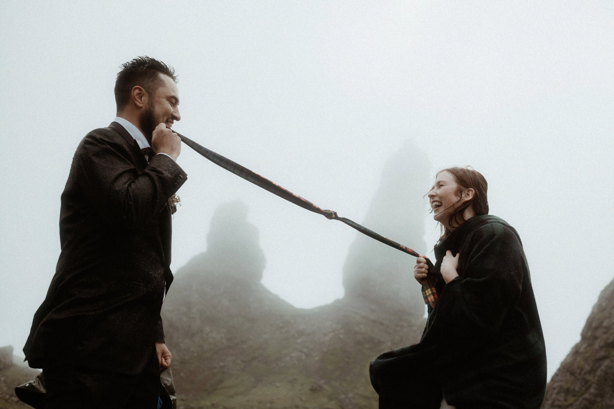 A traditional Scottish hand-fasting taking place during a wedding in Scotland outdoors in the rain with Bride and groom holding tartan ribbon near the Old man of Storr on Skye