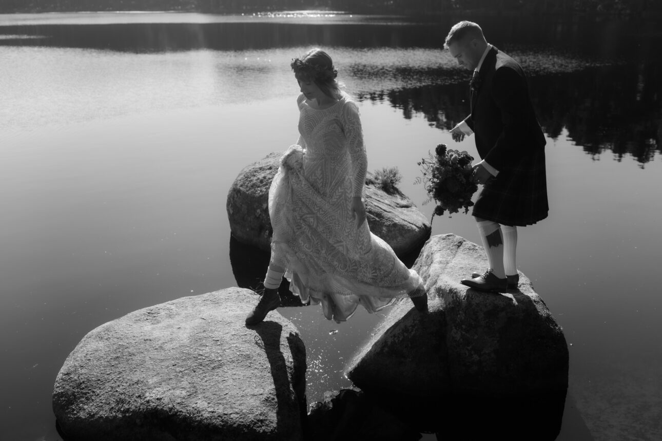 Bride and Groom jumping on rocks on Loch Garten in the Cairngorm's national park on a Sunny day during their elopement