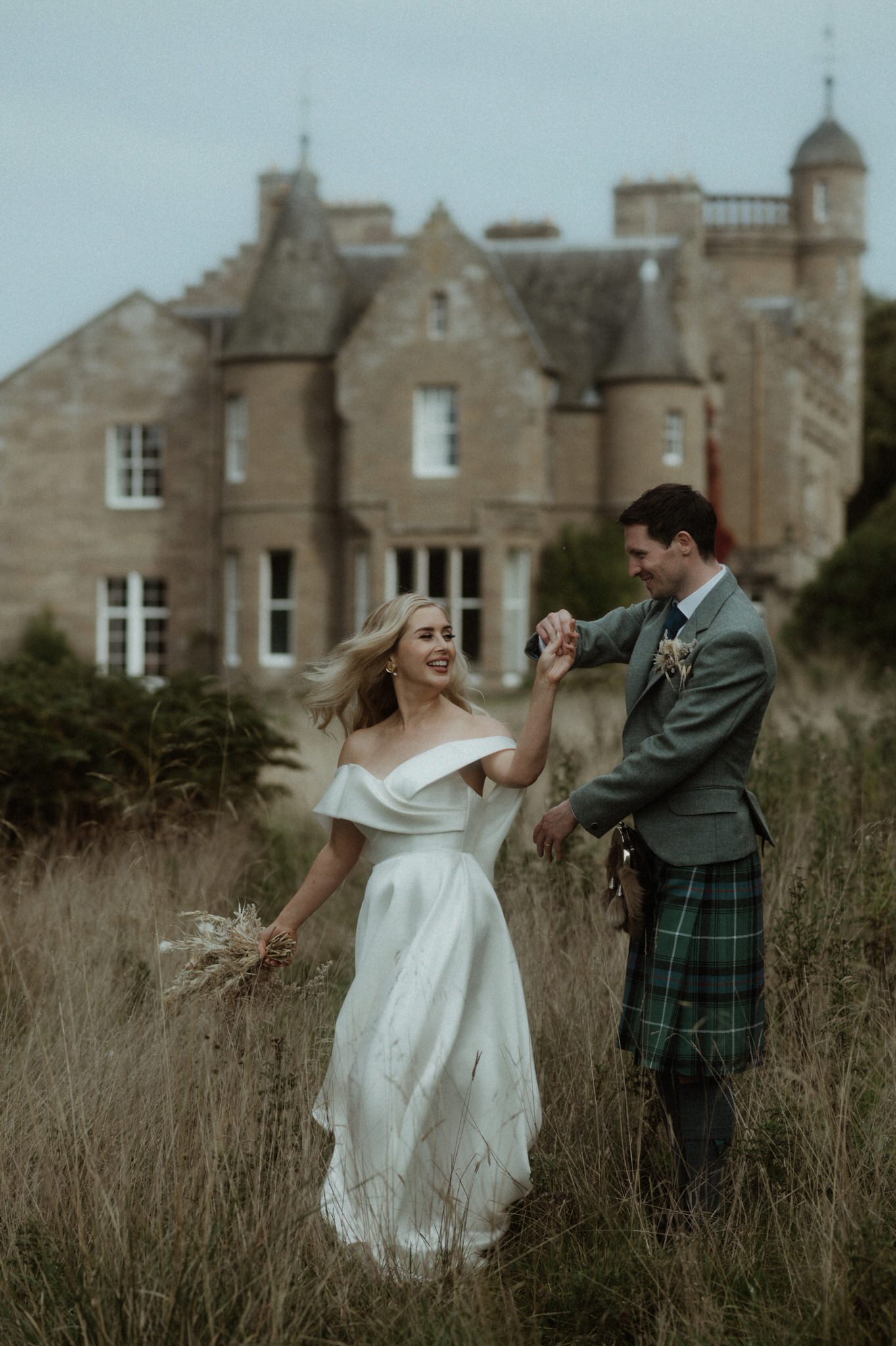 black and white image of bride and groom wandering next to Birkhill house in long grass kissing and laughing during their wedding in Scotland 