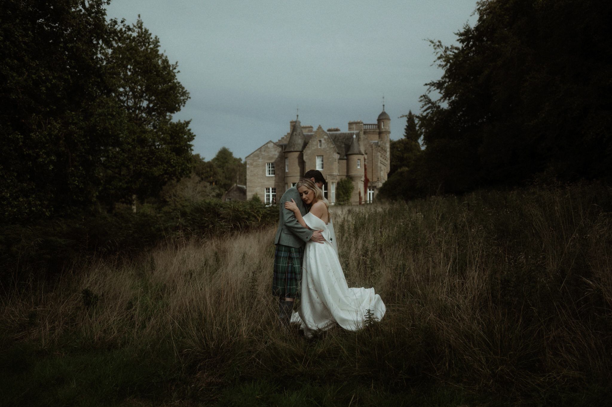 image of bride and groom wandering next to Birkhill house in long grass kissing and laughing during their wedding in Scotland 