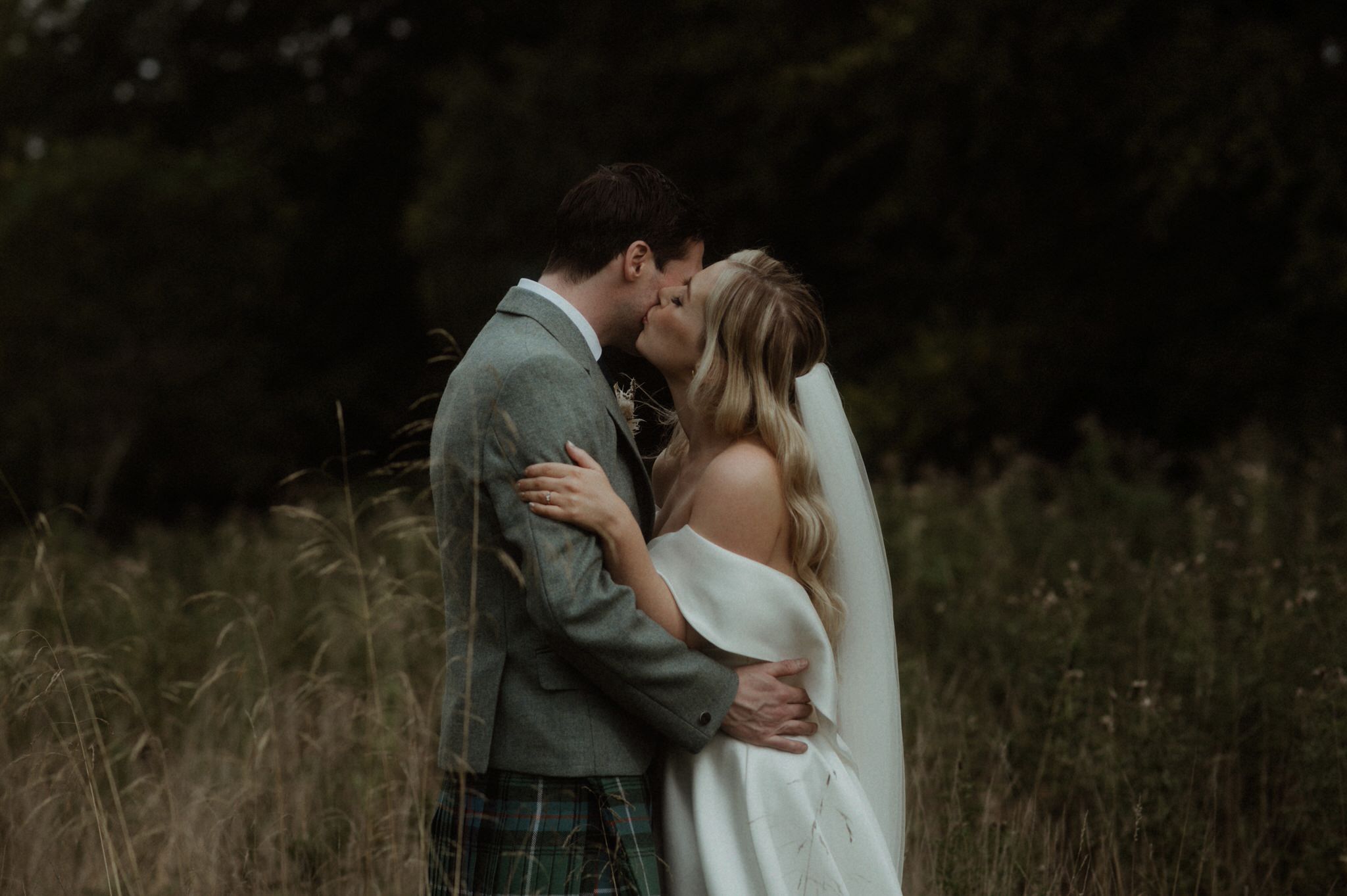 black and white image of bride and groom wandering next to Birkhill house in long grass kissing and laughing during their wedding in Scotland 