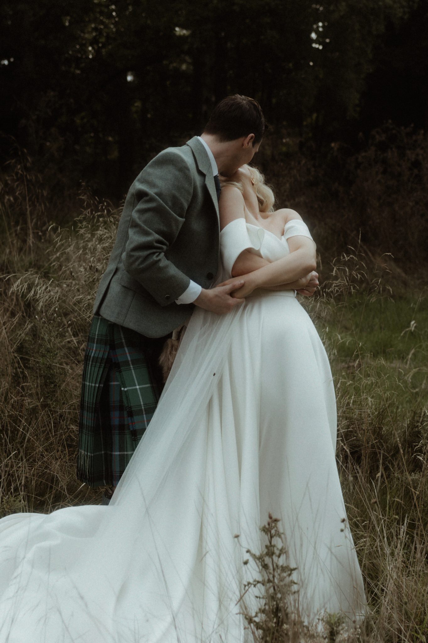 bride and groom wandering next to Birkhill house in long grass kissing and laughing during their wedding in Scotland 