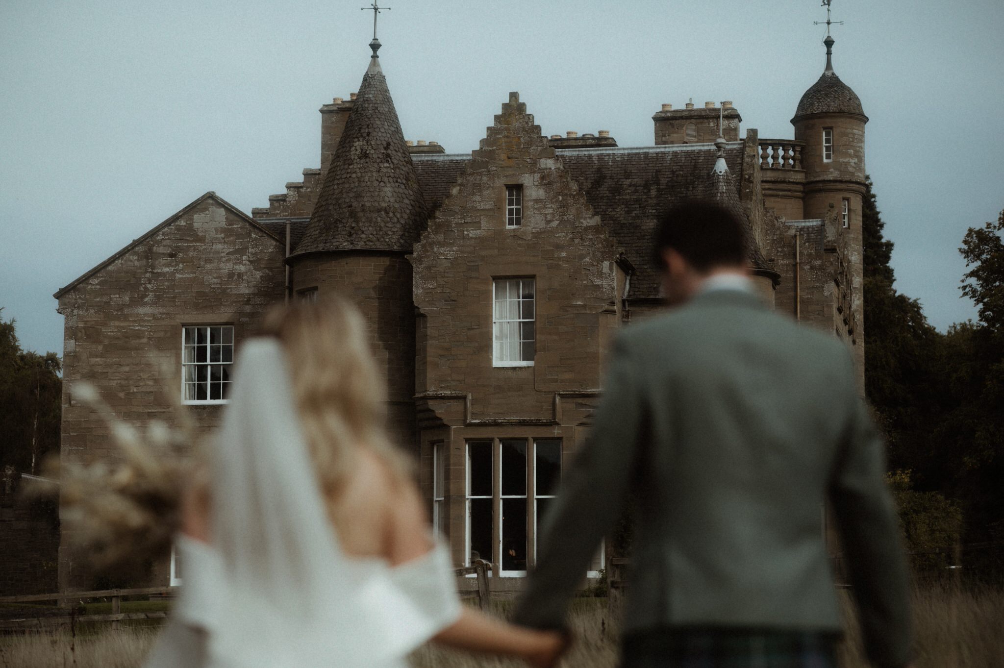 bride and groom wandering next to Birkhill house in long grass kissing and laughing during their wedding in Scotland 