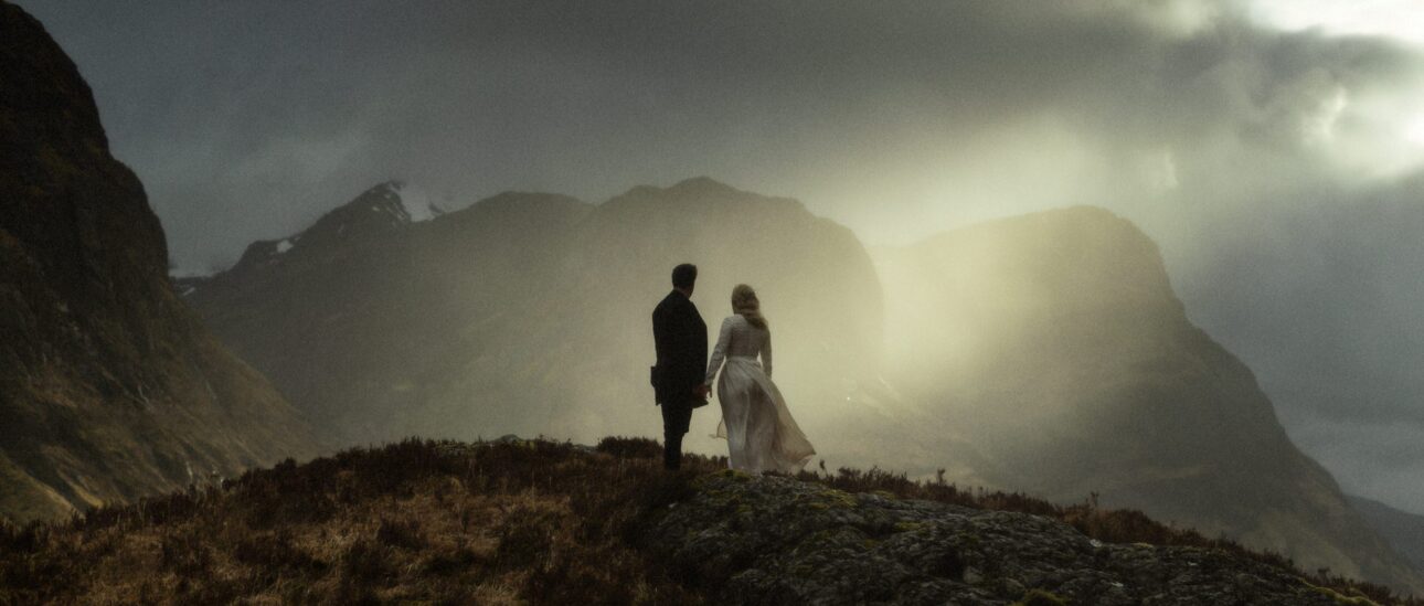 couple standing in the mountains of glencoe in scotland looking at the sunset