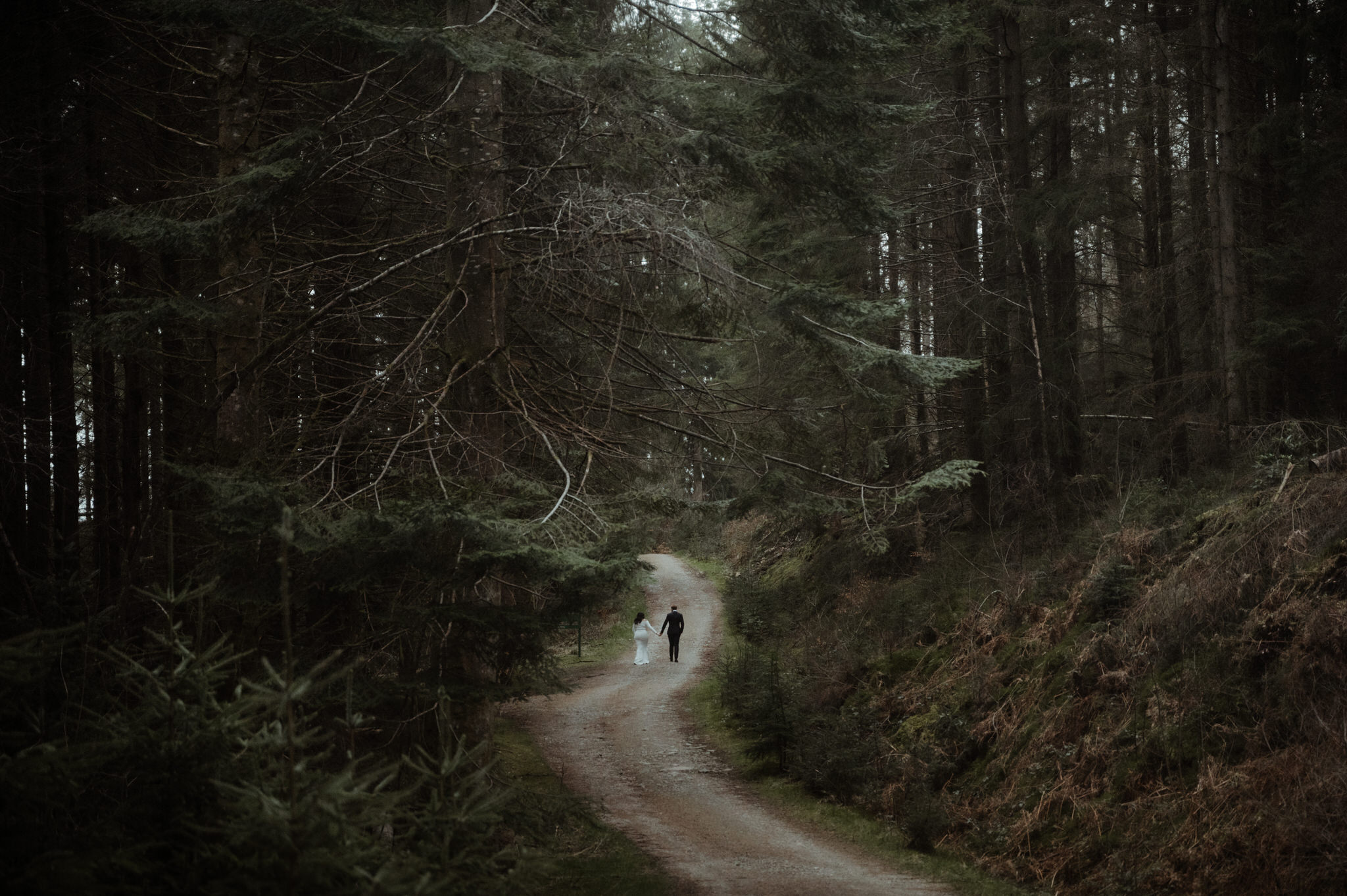 elope to scotland couple running on a road in a woodland