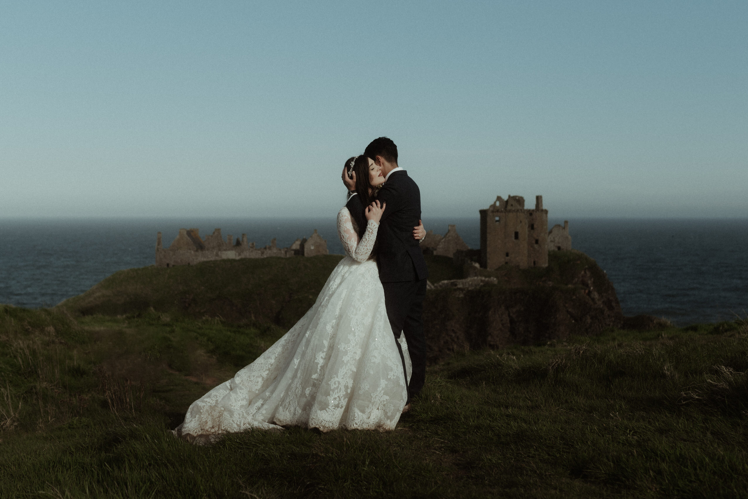 bride and groom hugging after their wedding in scotland in front of duntottar castle overlooking the cliffs and the North Sea