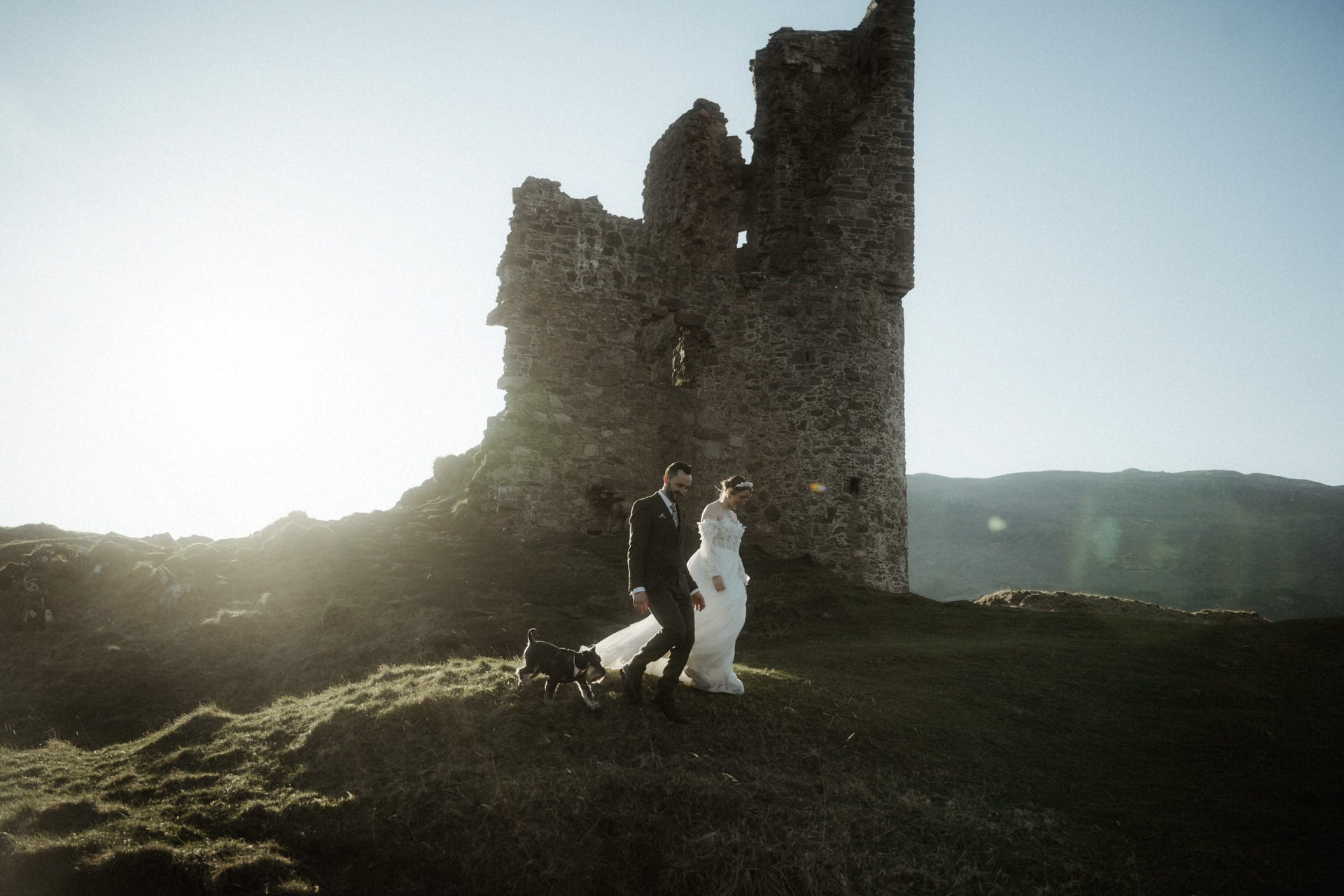 assynt elopement couple walking next to ardvreck castle in the sunlight with their dog